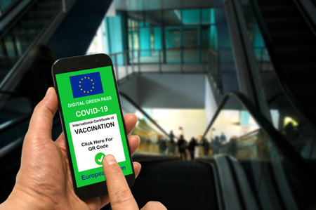 A man in a shopping mall holds a smartphone with the European Union digital green pass for Covid-19 in his hand. Safety concept for Coronavirus and the Green passの写真素材