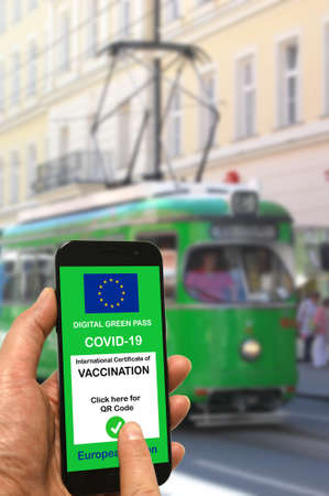 A man at a tram stop holds a smartphone with the European Union digital green pass for Covid-19 in his hand.の写真素材