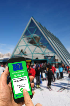 A man on a ski slope near the cable car station and ski lifts holds a smartphone with the European Union digital green pass for Covid-19 in his hand.の写真素材