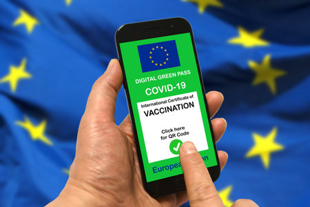 man hand's holding a smartphone with the digital green pass of the European Union with the QR code on the screen with a blurred EU flag in the backgroundの写真素材