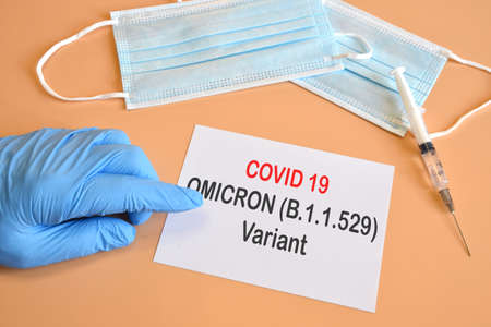 Covid-19 new Omicron variant. Doctor hand with blue glove indicate written "Covid-19 variant Omicron" on white paper. Medical face mask and vaccine syringe for covid 19. Protection concept for new Covid 19 Omicron variantの写真素材