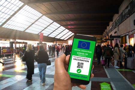 Man in a train station is holding smartphone with the European Union digital Green Pass for Covid-19 SARS-CoV-2. Safe travel concept during the Coronavirus and the Green Pass.の写真素材