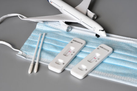 Covid travel safety concept. Airplane on protection mask with two SARS-CoV-2 Antigen Rapid Tests...