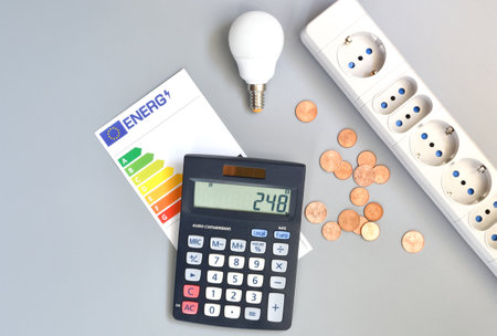 Energy efficiency rating table, light bulb, calculator, coins and power strip on gray background, close-up. Concept for increasing the price of energy.の写真素材