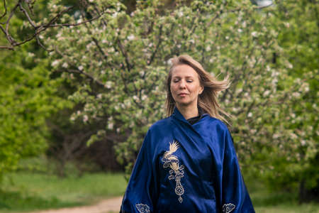 a woman in a blue kimono in a blooming Apple orchard poses next to an Apple treeの写真素材
