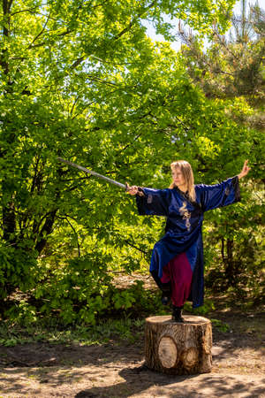 A girl in a blue kimono poses with a sword in the forest standing on a stumpの写真素材
