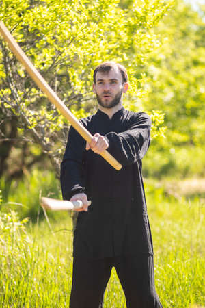 A young karate guy is engaged in Wushu with weapons in the Park. Practicing self-defense with sticksの写真素材