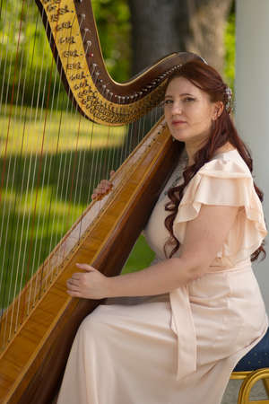 young woman in the woods is sitting next to a large harp. Classical music. Music and artの写真素材
