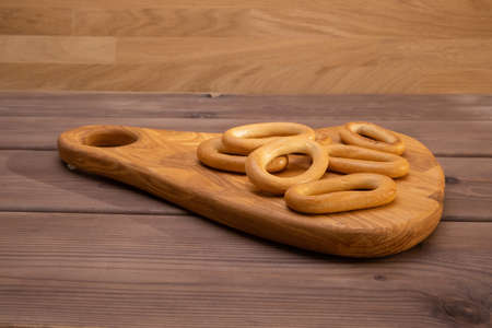 Dried bagels crackers lie on a wooden board on a wooden table. Snack for tea. Hard light