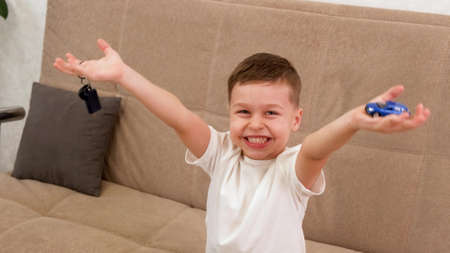 A happy boy holds a toy car and keys in his hands. The concept of buying a new car