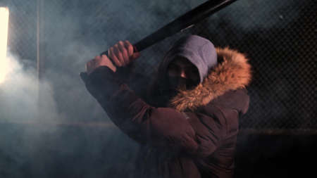 masked man strikes with a bat on a smoky street. The camera is moving towards him. Robber,...