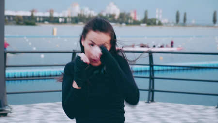 woman brunette Asian boxer punches the air on the sea pier. Shadow fight