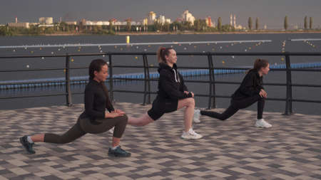 women in black tracksuits do a warm-up on the pier by the sea. Stretchingの写真素材