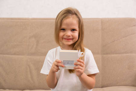 A little blonde girl is sitting smiling and holding a white boxの写真素材