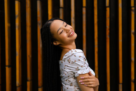 Portrait of a young pretty afro woman with pigtails who smiles and enjoys posing half sideways and hugs her handの写真素材