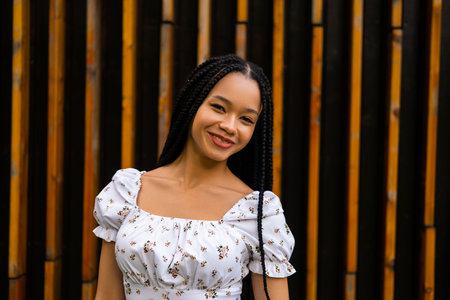 Portrait of a young pretty afro woman with pigtails who smiles beautifully and looks at the camera in a white dress with flowersの写真素材