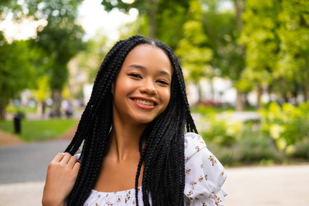 Portrait of a young beautiful African girl on the street in a summer light dress smiling and...