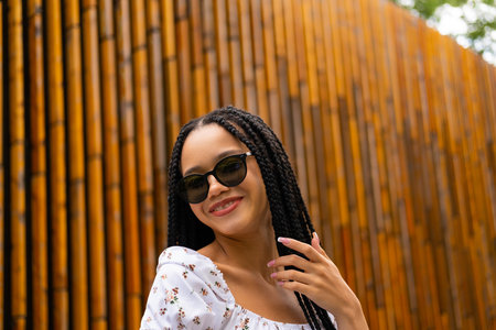 Young African woman in dark sunglasses smiling and looking at the camera on the street against the background of a wooden wall in the parkの写真素材