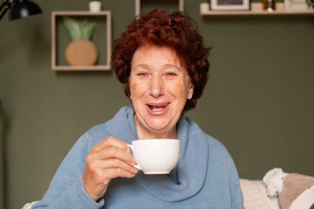 Portrait of an elderly woman with blue eyes looks at the camera and laughs with a cup of coffee in her handsの写真素材