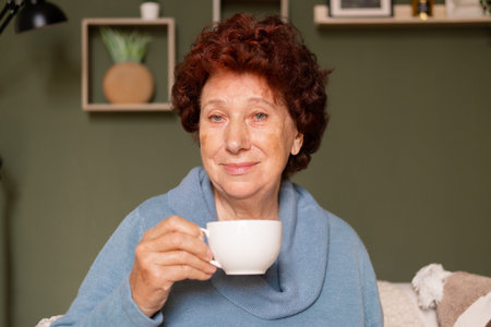 Portrait of an elderly woman with blue eyes looking at the camera with a cup of coffee in her handsの写真素材