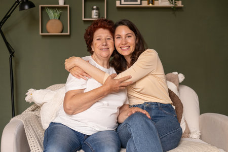 Portrait of a happy grandmother and granddaughter sitting on the sofa at home during the day, caring...
