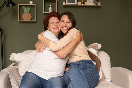 Portrait of a happy grandmother and granddaughter sitting on the sofa at home during the day, caring...