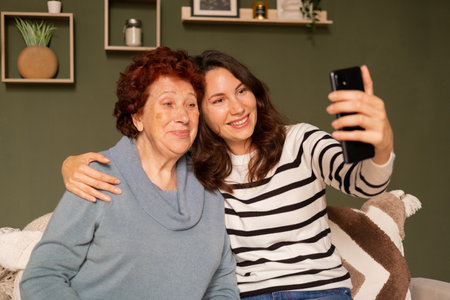 Portrait of a modern happy grandmother and granddaughter sitting on the sofa in the living room...