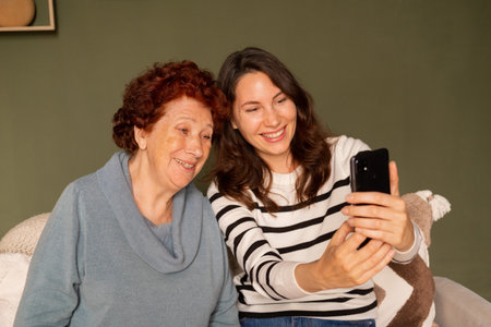 Portrait of a modern happy grandmother and granddaughter sitting on the sofa in the living room...