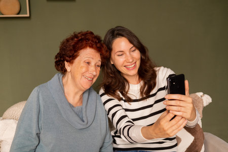 Portrait of a modern happy grandmother and granddaughter sitting on the sofa in the living room...