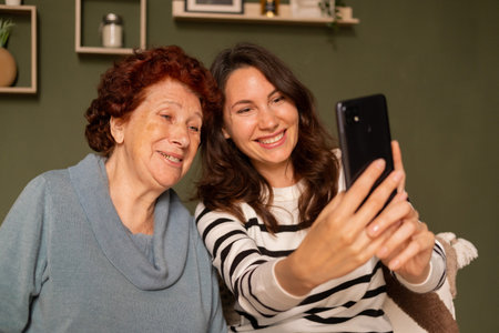 Portrait of a modern happy grandmother and granddaughter sitting on the sofa in the living room...