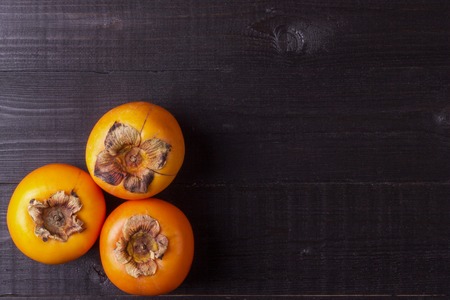 Fresh persimmons on black wooden surfaceの写真素材