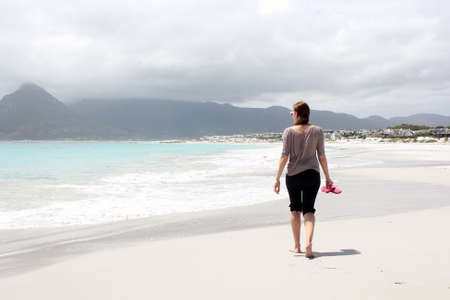 Woman walking along the Beach of Kommetjie with an upcoming storm in the backgroundの写真素材