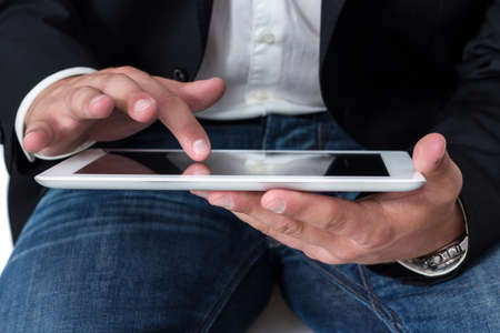 A Man with blue jeans working on a tablet pc with he's handの写真素材