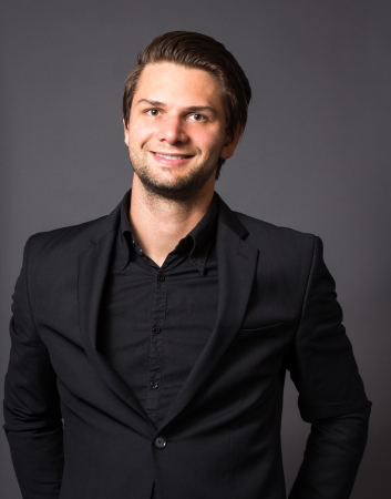 Man in Black Suit in front of a grey background looking happyの写真素材
