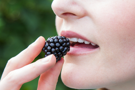 Caucasian woman putting blackberry into mouth closeupの写真素材
