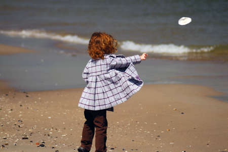 A little girl standing on a beach throwing a sea shell into the waterの写真素材