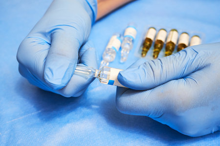 Hands of a nurse in blue gloves open an ampoule with medicine close-upの写真素材
