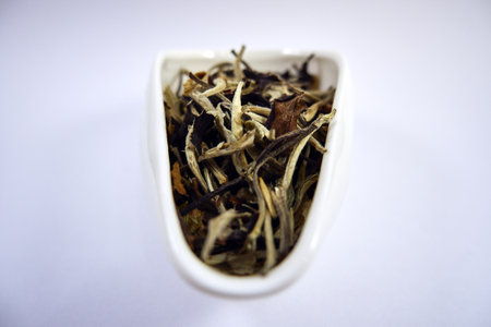 Dry tea leaves in a white cup on a white background.