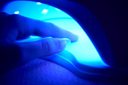 Close-up of a woman's hand under an ultraviolet lamp. Gel polish for nails. Beauty salon and beautician appointment conceptの写真素材