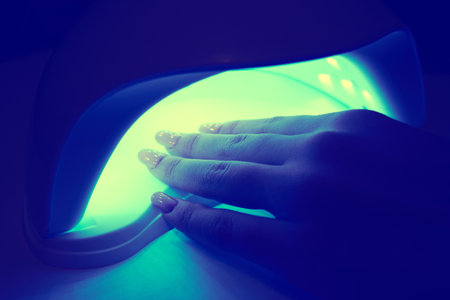 Girl's hand inside an ultraviolet lamp for drying nail polish close-up. Color toning appliedの写真素材