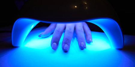 Woman's hand inside lamp for drying nail polish on table close-up. UV lamp for drying nail polishの写真素材