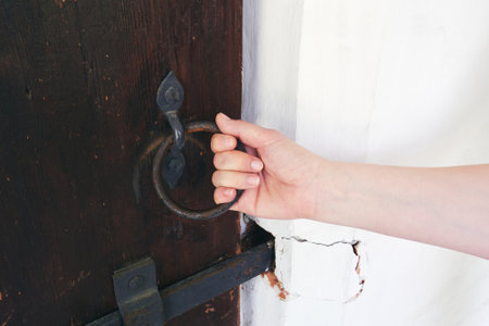 Female hand opens an ancient door. Vintage iron door handle in the form of a ring. Toned imageの写真素材