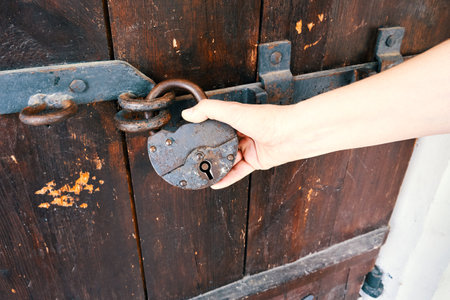 Old wooden door with rusty lock. Close-up of female hand holding a padlockの写真素材