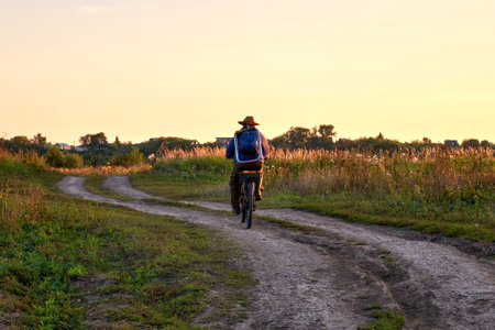 Cyclist riding on a dirt road in the field at sunset. A man rides home on a bicycleの写真素材