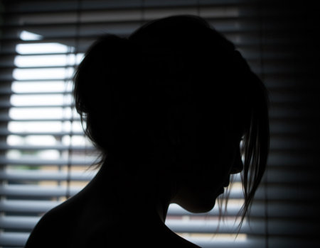 Silhouette of a girl in a window with blinds, head close-upの素材