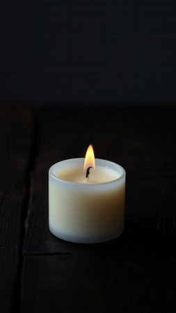 A lone white candle on a dark wooden tableの素材