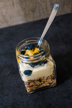A jar of healthy swiss museli, yogurg, blackberries and honey on a black slate background