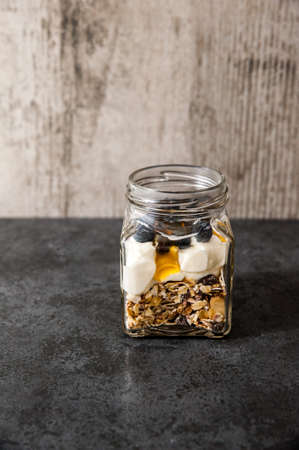 A jar of healthy swiss museli, yogurg, blackberries and honey on a black slate backgroundの写真素材