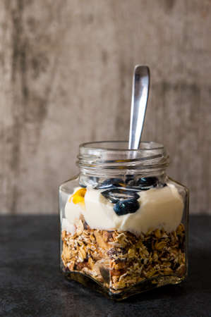 A jar of healthy swiss museli, yogurg, blackberries and honey on a black slate backgroundの写真素材