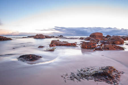 Long exposure photography of waves crashing over rocks at sunrise with storm clouds buildingの写真素材